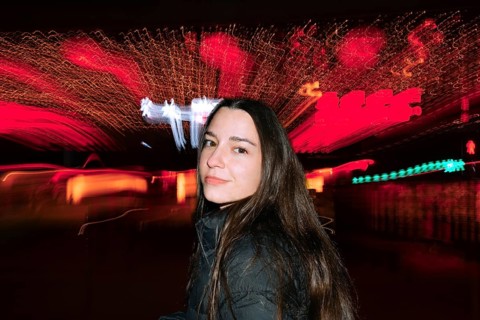 A woman with long hair poses at night with a dynamic backdrop of colorful motion blur, creating a