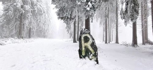 Snowy hiking trail on the Rennsteig with an icy stone with the letter R as a signpost that conveys