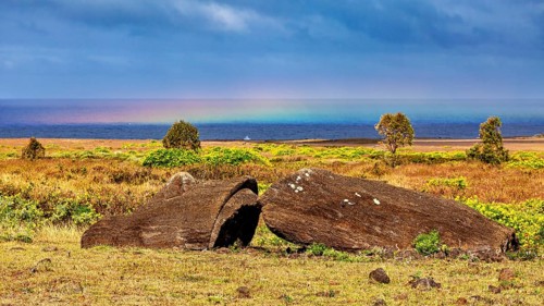 Boulders in a dry meadow with rainbows over the sea, The Moai statues on Easter Island in the