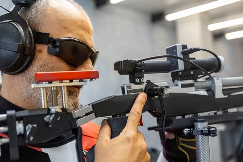 A visually impaired athlete intensely focusing on target shooting. They are using assistive