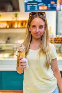 Vertical portrait of a blonde chic woman eating ice cream cone in store