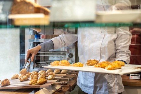 Baker in white uniform arranging golden brown empanadas with tongs on a wooden board and tray in a