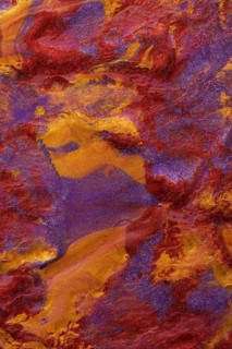 Close-up view of a vibrant, abstract metallic paint blend of red, purple, and gold hues. Ideal for