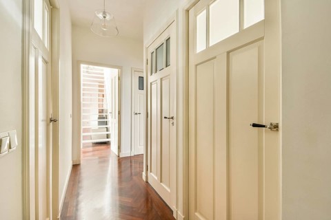 A well lit hallway featuring polished wooden flooring and several white panel doors, accented by a