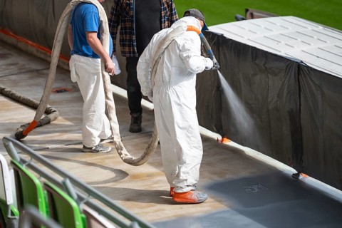Manual workers perform pressure spraying of polyurea resin on the concrete of the stadium stand