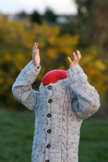A young unrecognizable child, hiding while wearing a whimsical red hat and textured gray sweater,
