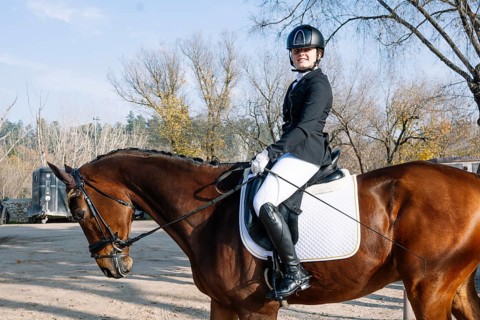A rider elegantly dressed in classical dressage attire, including a helmet and riding boots, sits