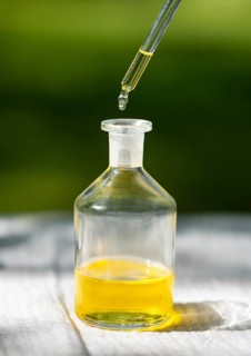 A pipette dispensing oil into a small glass bottle, set against a softly focused green background.