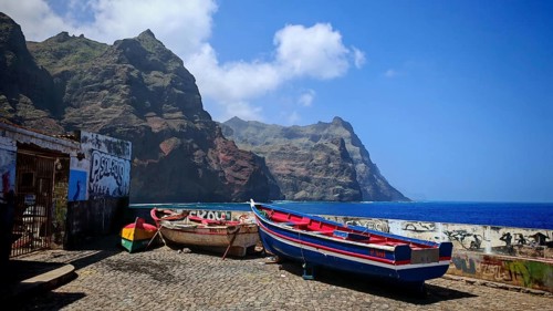 Colourful fishing boats in front of a wall with graffiti on a rocky coastal strip with majestic