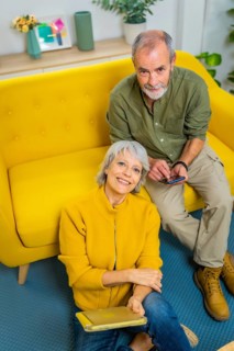 Vertical top view portrait of a senior couple relaxed at home together holding mobile phone and
