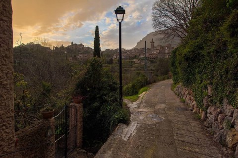 A scenic pathway in Valldemossa, Spain, during sunset showcases the village's charming architecture