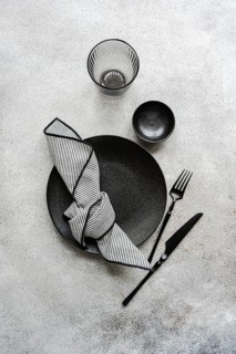 A sophisticated black and white table setting features a textured plate, stylish glassware, striped
