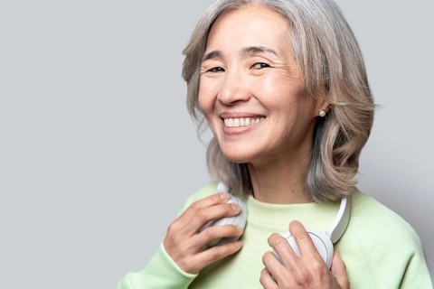 Asian Chinese senior woman with gray hair smiling warmly, wearing a light green sweater, holding