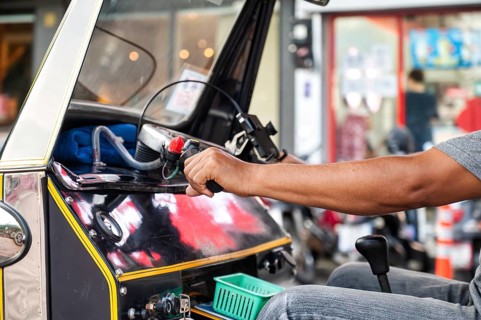 Cropped unrecognizable male Thai tuk tuk driver navigating a black vehicle through the bustling
