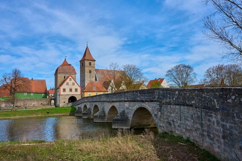 Historic stone bridge leads across river to a village with a distinctive church and towers, spring,