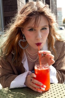 A woman with stylish accessories, including large hoop earrings and layered necklaces, sips a