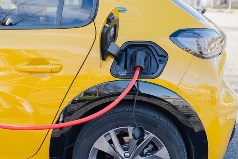 A vibrant yellow electric car is connected to a charging station via a red cable. The focus is on