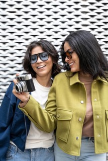 Two women share a joyful moment, posing with a vintage camera. They are smiling and wearing casual