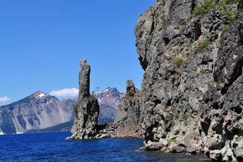 Rocks at the edge of a lake with a mountain range in the background under clear sky, Crater Lake