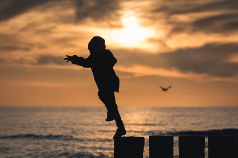 Silhouette of boy jumping from breakwater during sunset