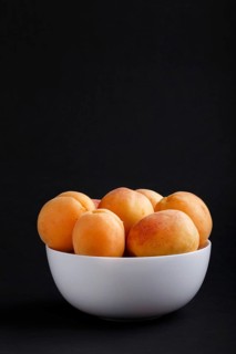Fresh orange apricots in white bowl on black background. side view, copy space