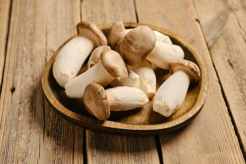 A round wooden plate filled with king oyster mushrooms. The scene shows a wooden table surface with