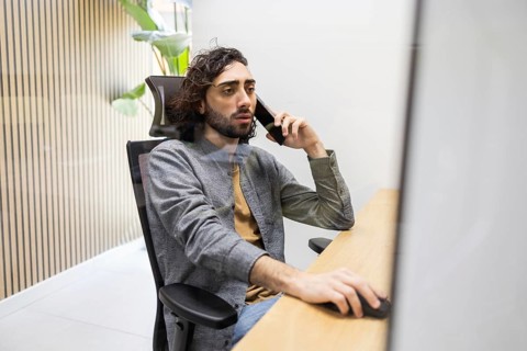 A focused professional sits at a sleek office desk, multitasking with a phone call while using a