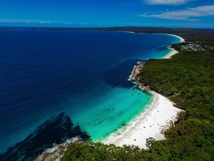 Aerial view of a pristine coastline with turquoise waters and white sandy beach, bordered by lush