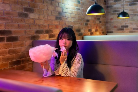 Asian Gen Z girl enjoying pink cotton candy Warm ambient lighting and brick walls create a relaxed
