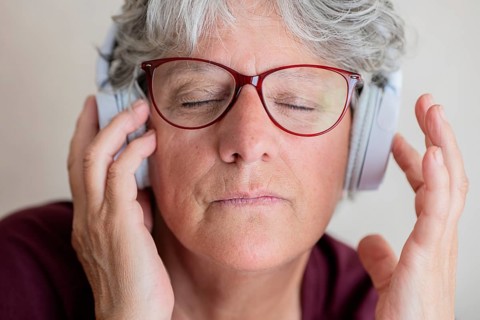 An senior woman with red glasses and silver hair enjoys music with closed eyes, fully immersed in