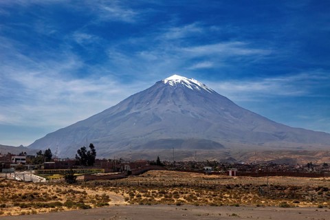 A snow-covered volcano rises majestically under a clear blue sky with light clouds, volcano in the