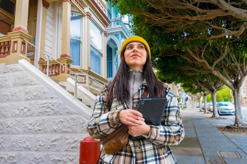 Woman traveler wearing a yellow beanie and plaid coat exploring the historic victorian houses of