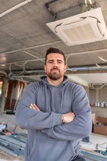 Hvac technician standing with arms crossed at a construction site, overseeing the installation of a