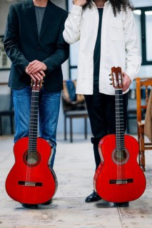 Anonymous portrait of confident male artists carrying red bass guitars in music studio