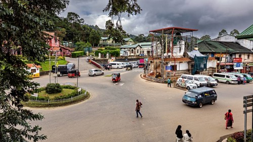 Roundabout with cars and people surrounded by buildings, under cloudy sky, Nuwara Eliya Sri Lanka