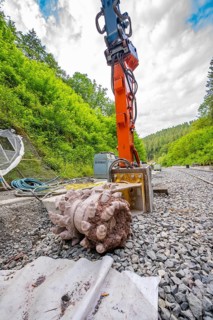 Large machine and tools on a railway construction site in a green, wooded environment, track