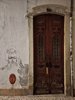 Framed wooden door with decorated relief, next to a portrait sketch on the wall, Lagos, Algarve,