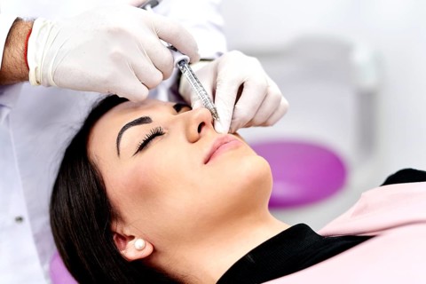 A woman receives a facial cosmetic surgery treatment in a clinical environment. A professional