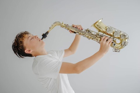 A young musician dressed in a white shirt passionately plays the saxophone. Eyes closed, he is
