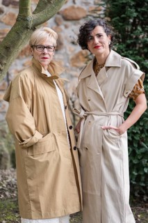 Two fashion women in stylish trench coats pose outdoors. They exude confidence and elegance amid a