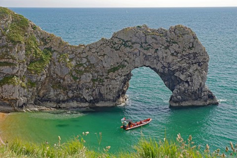 Boat in the turquoise blue sea in front of dramatic rock arches on the coast, Durdle Door,