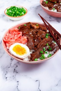 Gyudon Japanese beef with rice, pickled ginger, boiled egg slice, garnished with green onions, in a
