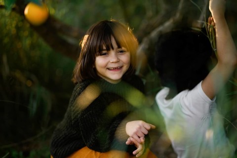 Joyful children with dark hair smiles warmly while playing outdoors on a sunny day, surrounded by