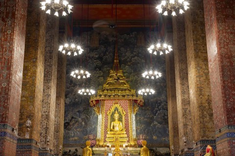 Golden meditating Buddha surrounded by wall paintings with Buddhist teachings and representations