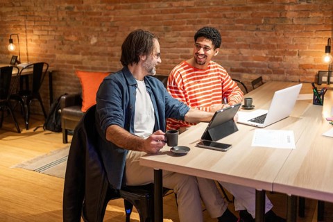 Two colleagues engage in a productive discussion at a coworking space. Laptops and coffee cups on