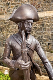 Bronze statue of a soldier in historic clothing in front of a stone wall, statue in the historic