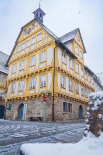 A large, yellow-painted half-timbered house with historical significance in the snow-covered city
