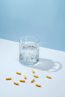 Yellow capsules spilled next to an elegant crystal glass of water, set against a soft blue