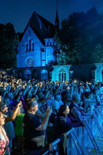 Crowd at night concert in front of a church, many holding up mobile phones, blue lighting,