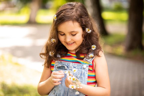 A cheerful little girl with a vibrant smile enjoys the outdoors, adorned with chamomile flowers in